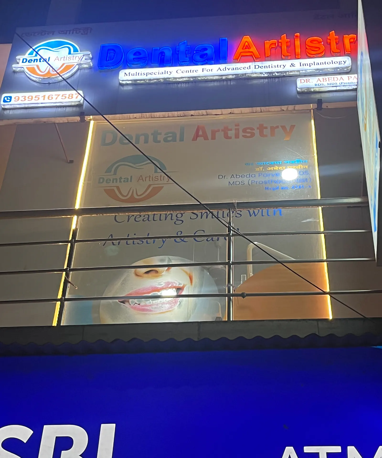 The Dental Artistry frontage at night: a lit sign above first-floor windows, with an SBI ATM sign at street level